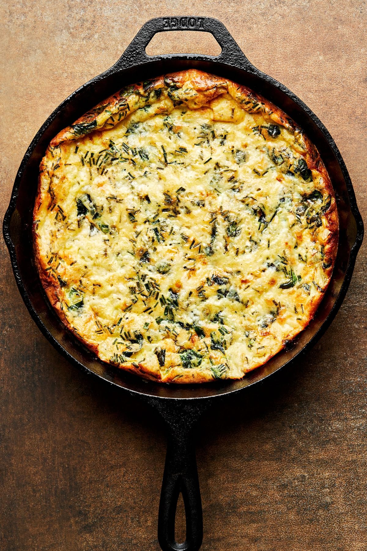 a homemade frittata fresh out of the oven in a cast iron skillet made with eggs, milk, cheese, vegetables and spices