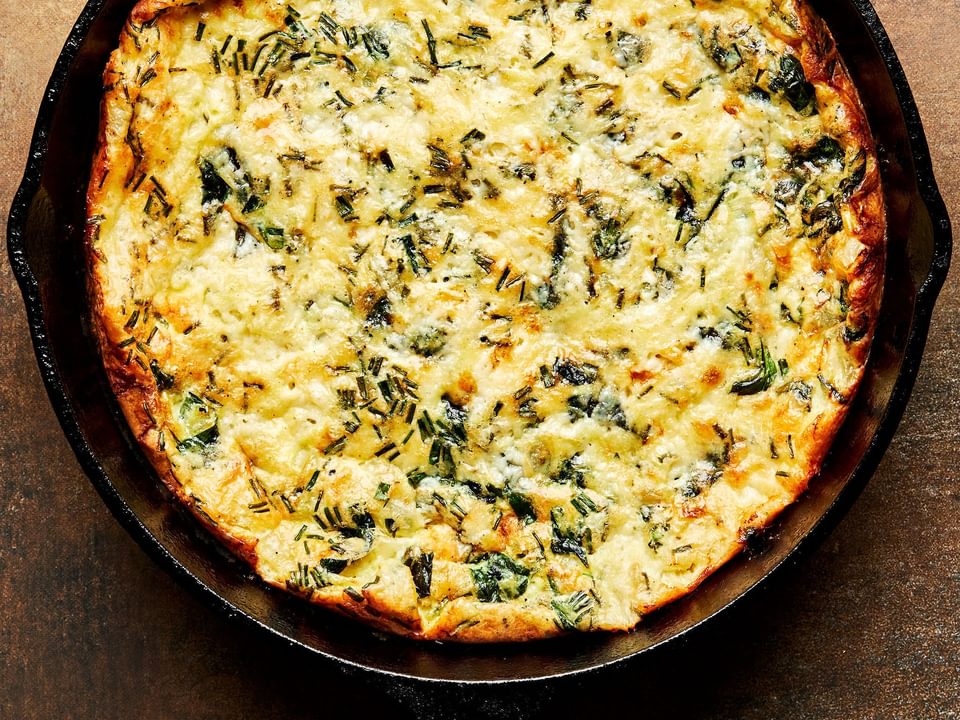 a homemade frittata fresh out of the oven in a cast iron skillet made with eggs, milk, cheese, vegetables and spices