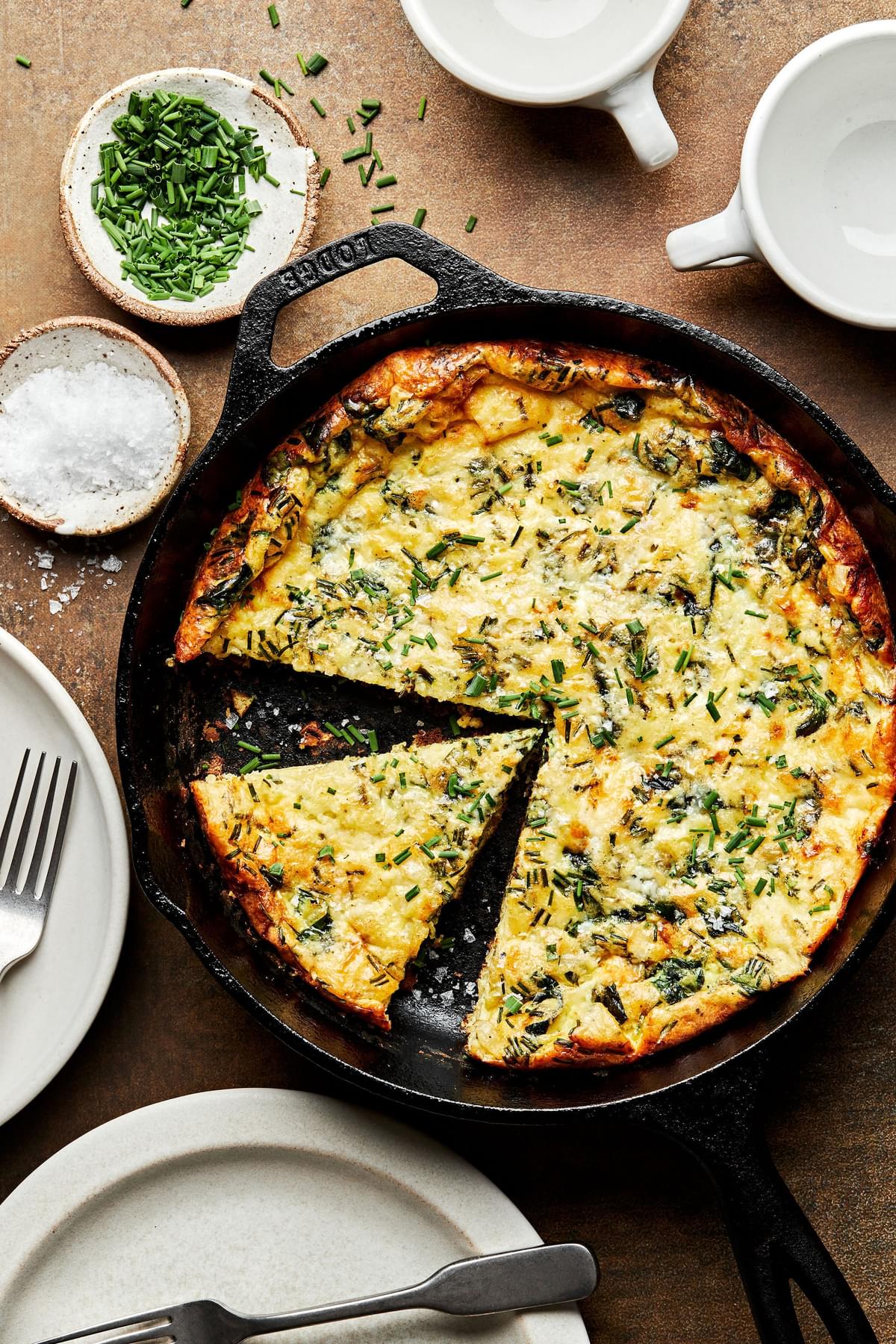 a homemade frittata in a cast iron skillet with a slice cut out made with milk, eggs, cheese, herbs, spices and cheese