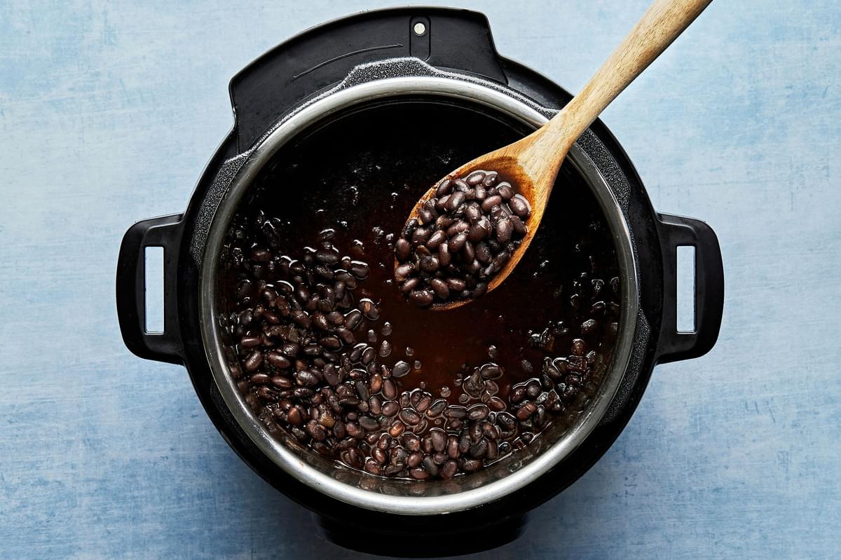 homemade instant pot black beans in an instant pot being scooped with a wooden spoon