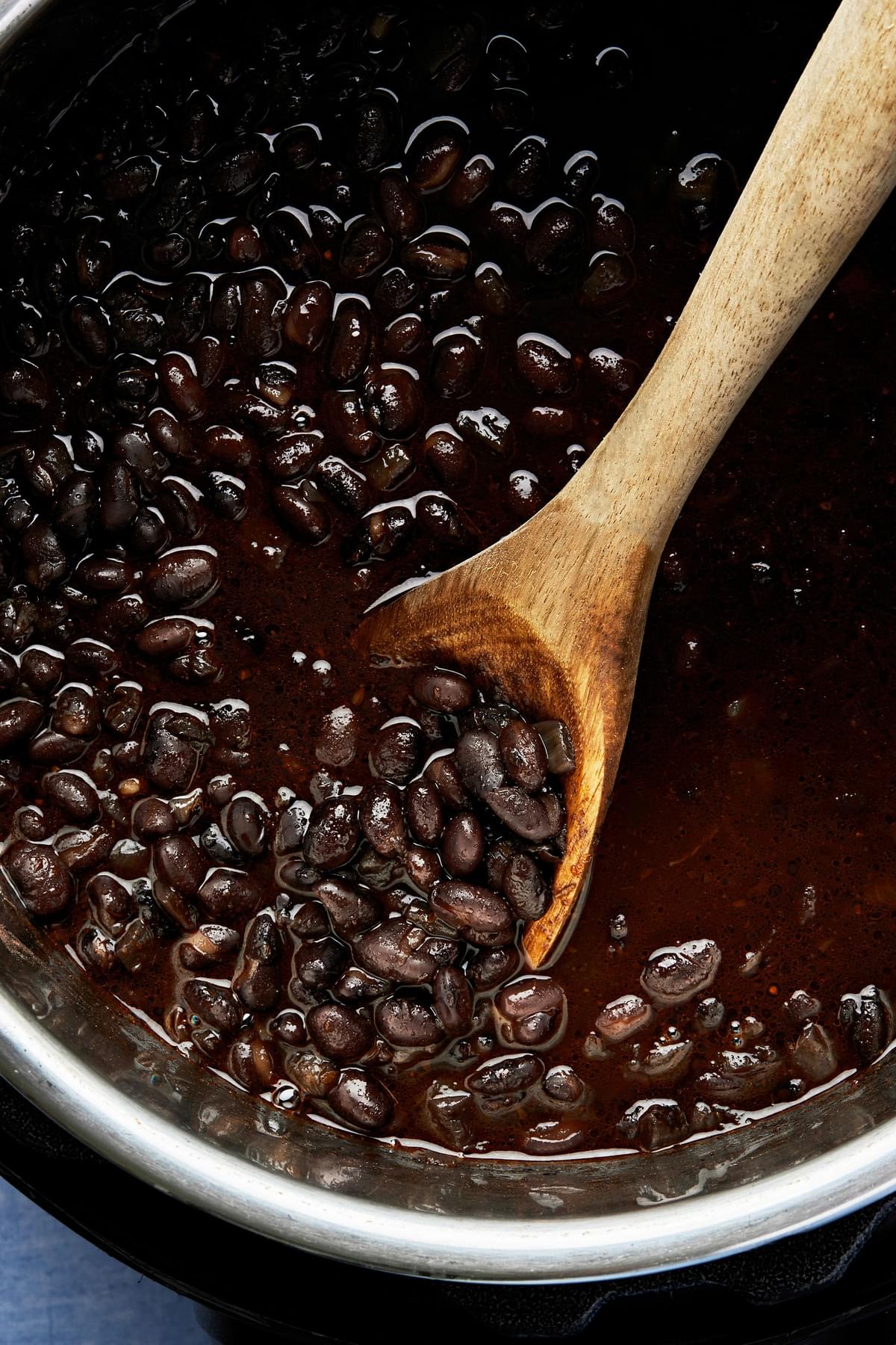 homemade black beans in an instant pot being stirred with a wooden spoon