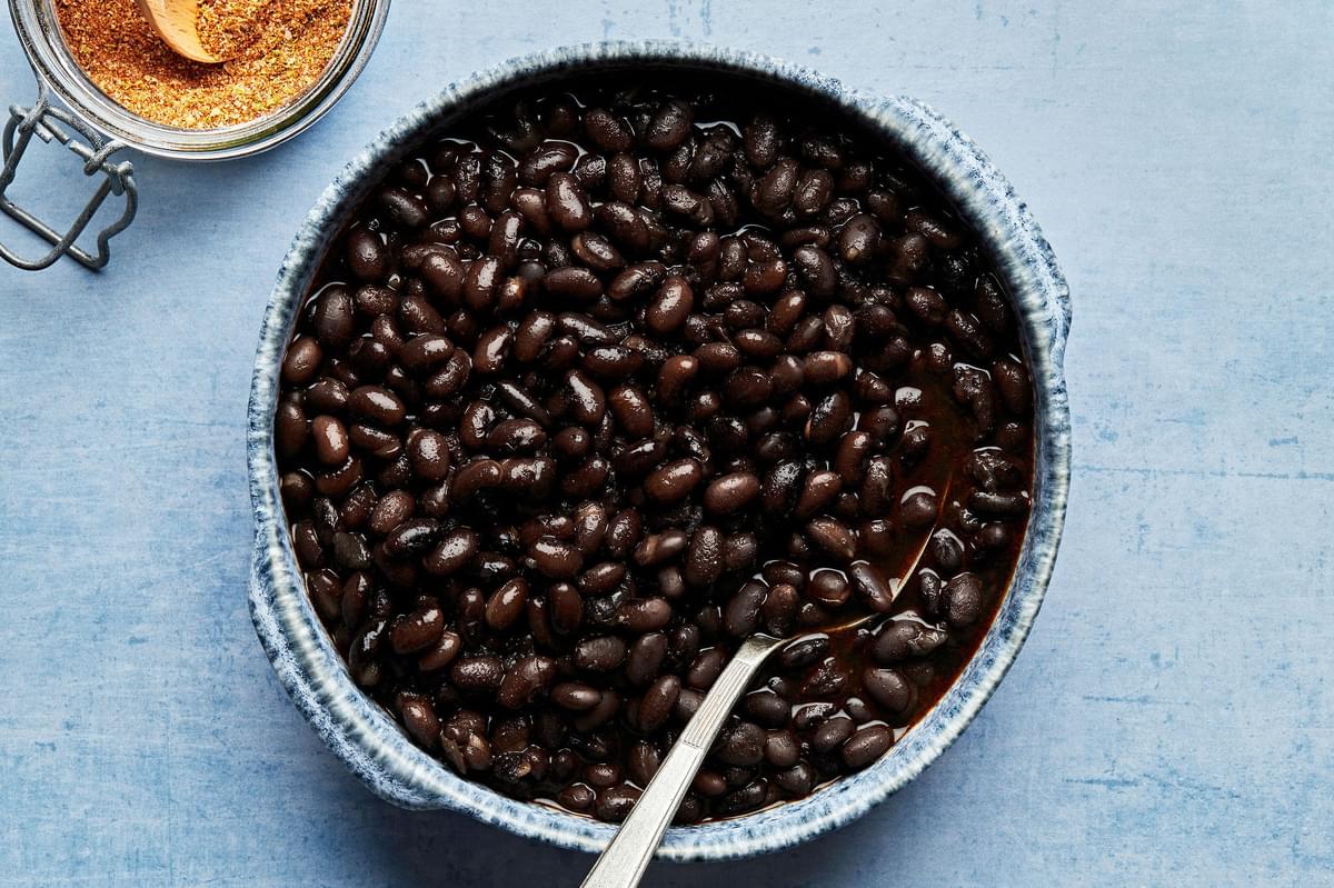 a bowl of homemade black beans in a bowl with a spoon next to a jar of homemade taco seasoning
