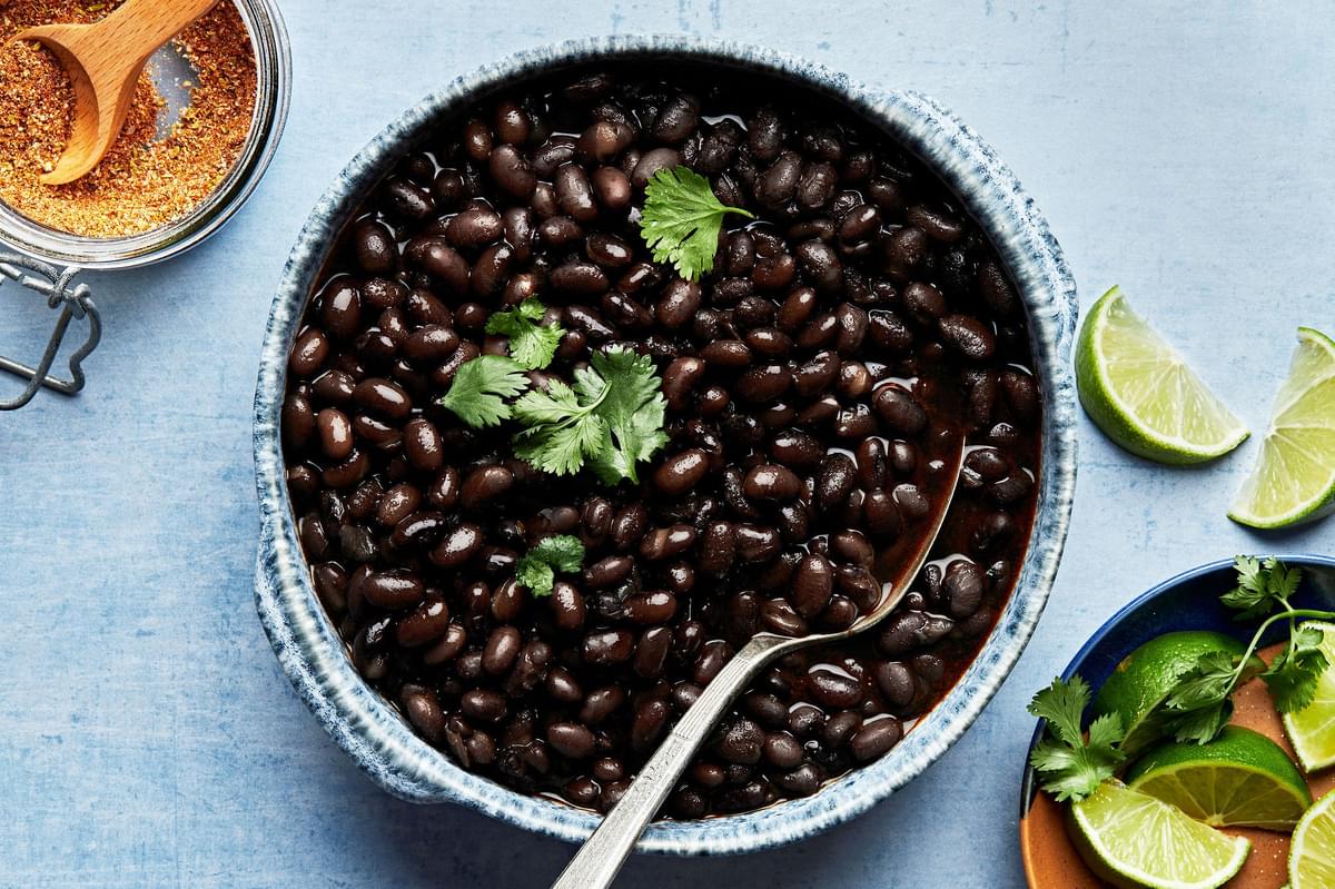 instant pot black beans in a bowl with a spoon topped with cilantro and next to bowl of lime wedges and taco seasoning