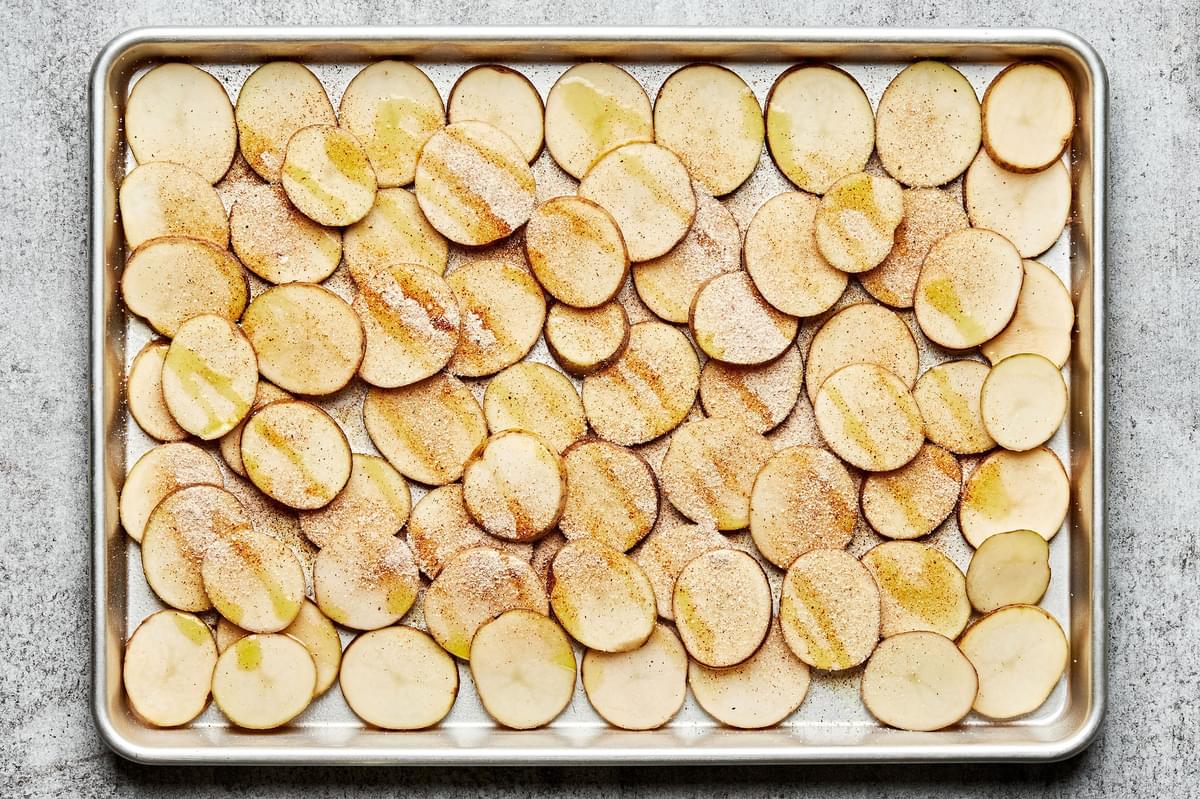 thinly sliced potatoes on a baking sheet drizzled with olive oil and sprinkled with garlic, onion and chili powders and salt