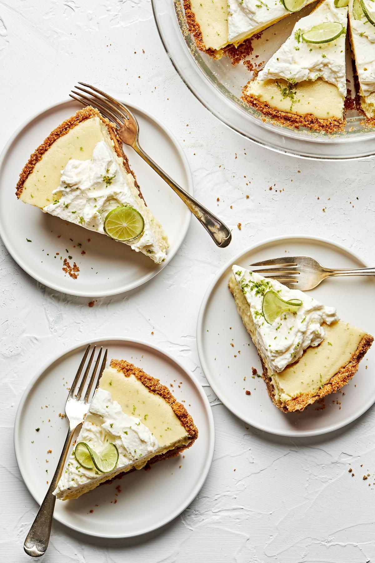 slices of homemade key lime pie on plates with graham cracker crust and topped with whip cream and slices of key lime