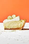 a slice of homemade key lime pie with graham cracker crust and topped with whip cream and slices of key lime
