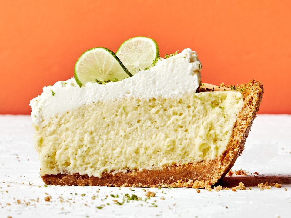 a slice of homemade key lime pie with graham cracker crust and topped with whip cream and slices of key lime