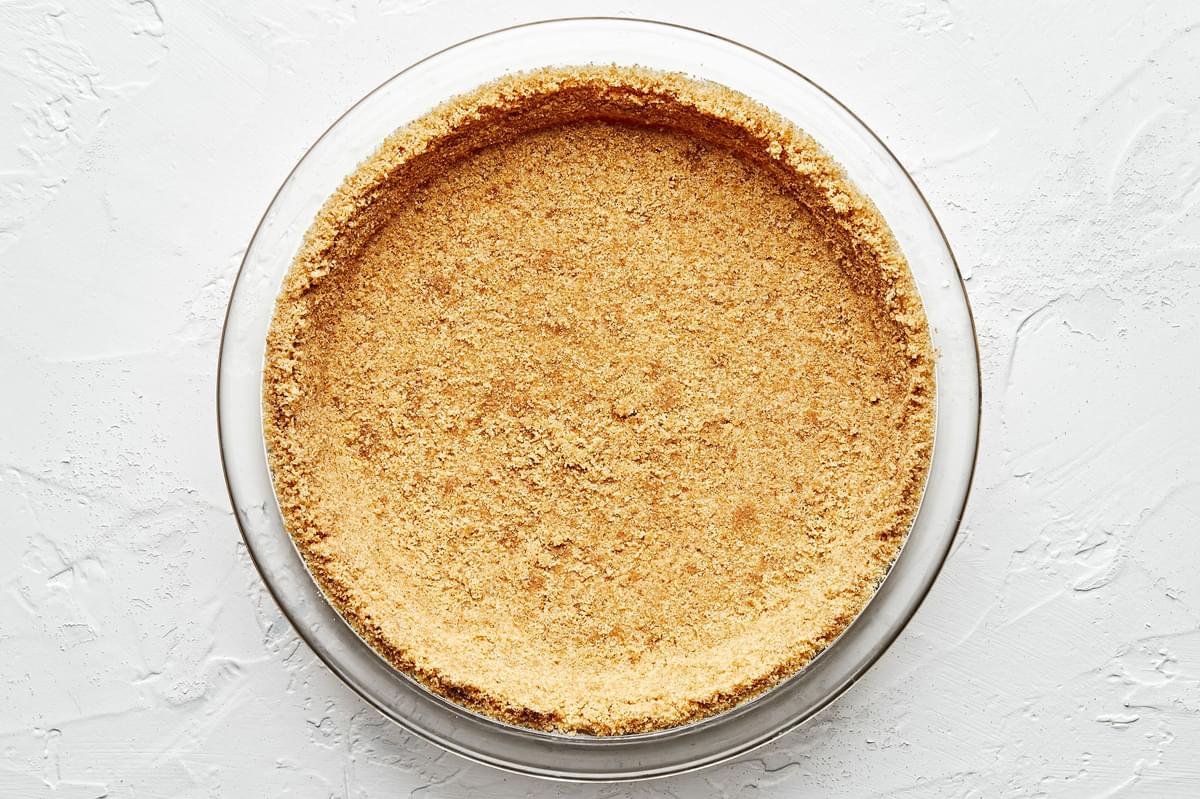 raw homemade graham cracker crust in a glass pie pan made with graham cracker, butter and sugar
