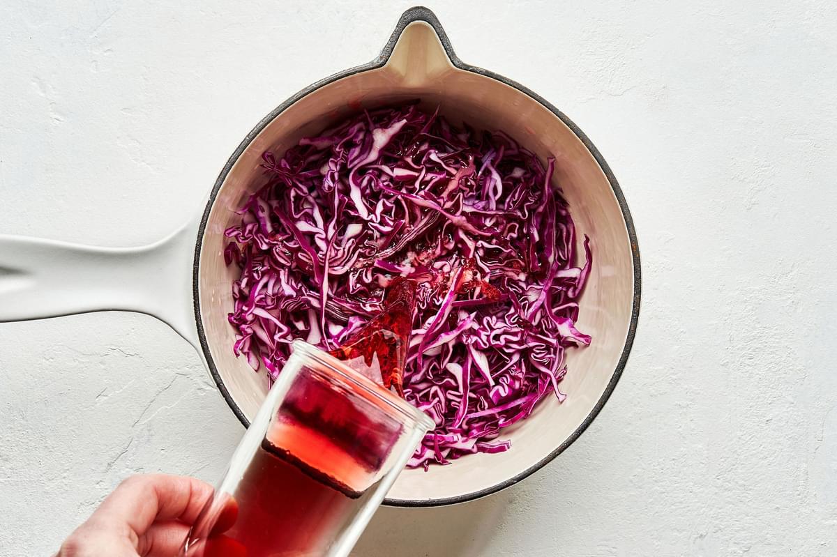 red wine vinegar and apple cider vinegar being poured over shredded red cabbage in a saucepan to make pickled red cabbage