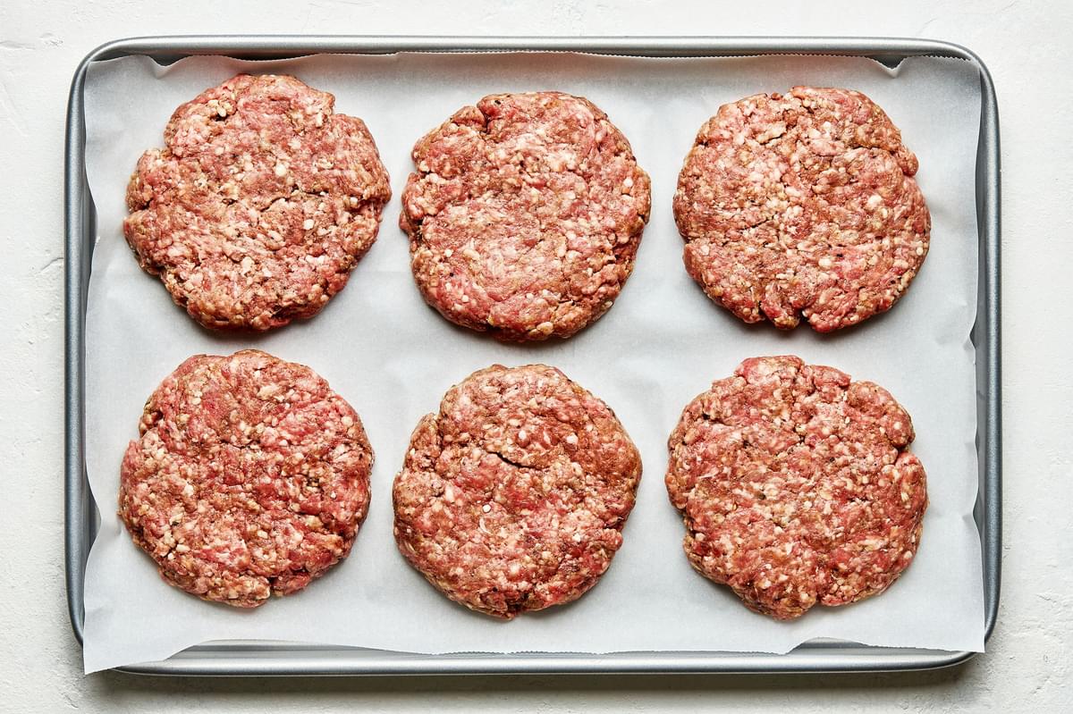 lamb burger patties on a parchment-lined baking sheet seasoned with Worcestershire, onion & garlic powders, salt & pepper
