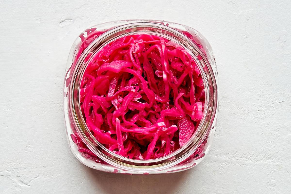 a jar of homemade picked red cabbage on the counter for hamburgers with harissa may and pickled red cabbage