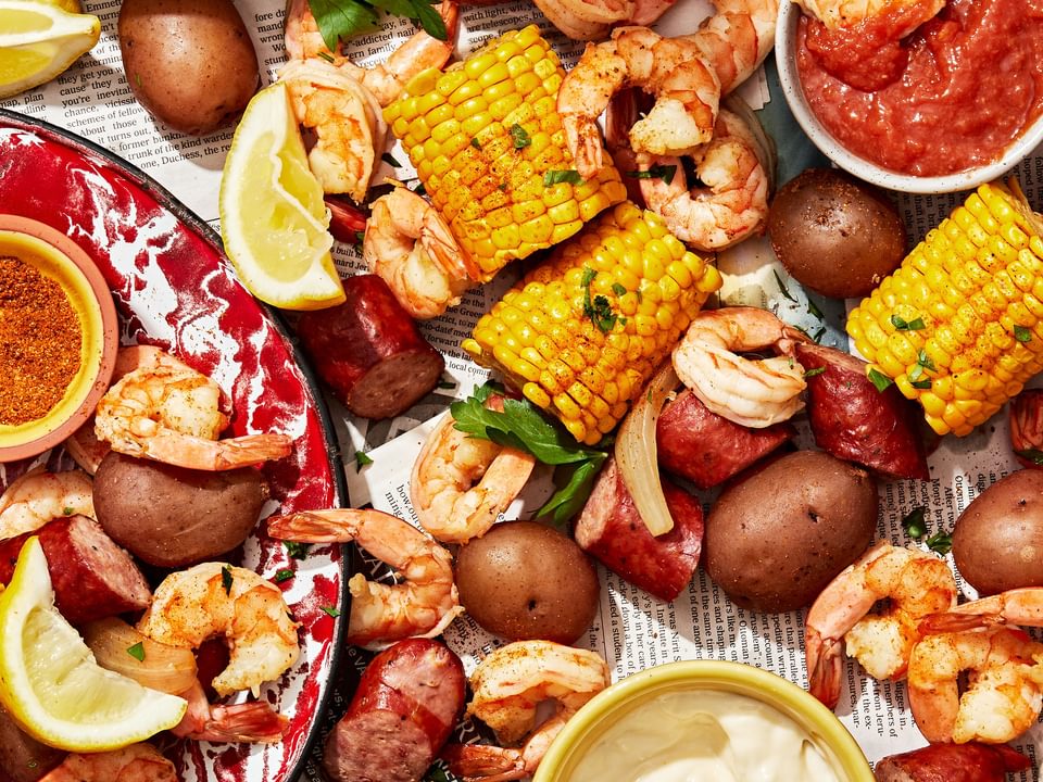 low country boil made with corn, shrimp, potatoes and sausage spread out on a table with sauces for dipping