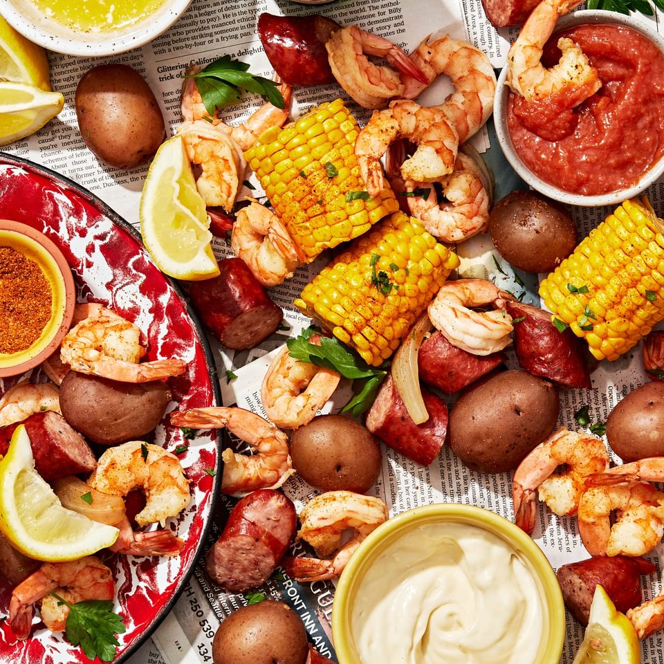 low country boil made with corn, shrimp, potatoes and sausage spread out on a table with sauces for dipping