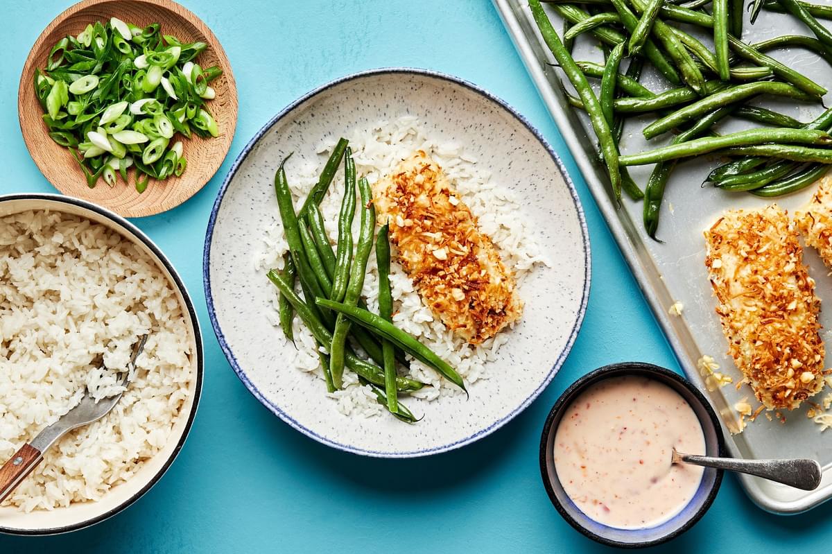 a bowl of coconut ginger rice with green beans and macadamia nut crusted fish next to sweet chili mayo sauce for drizzling