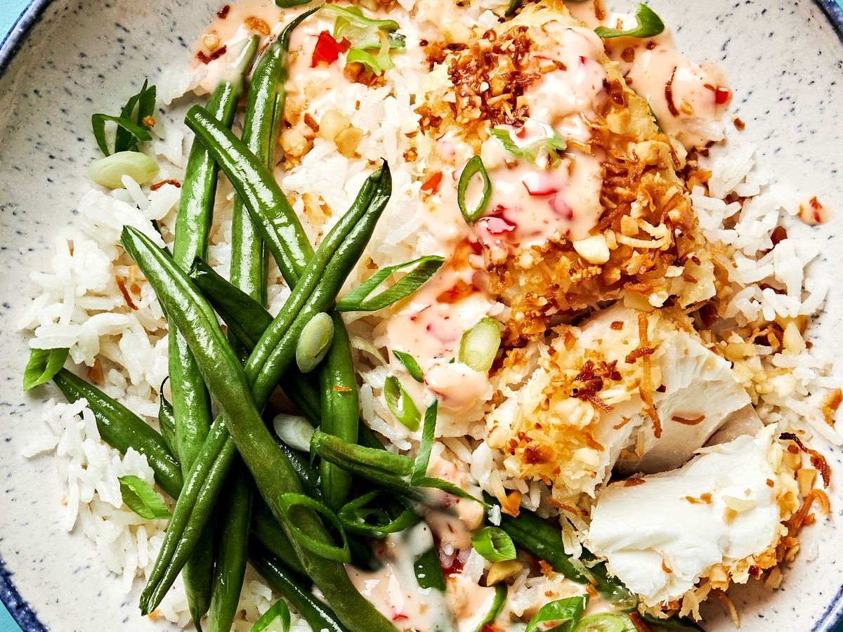 A macadamia nut crusted fish bowl with coconut rice, green beans and a sweet chili mayo sauce drizzled on top