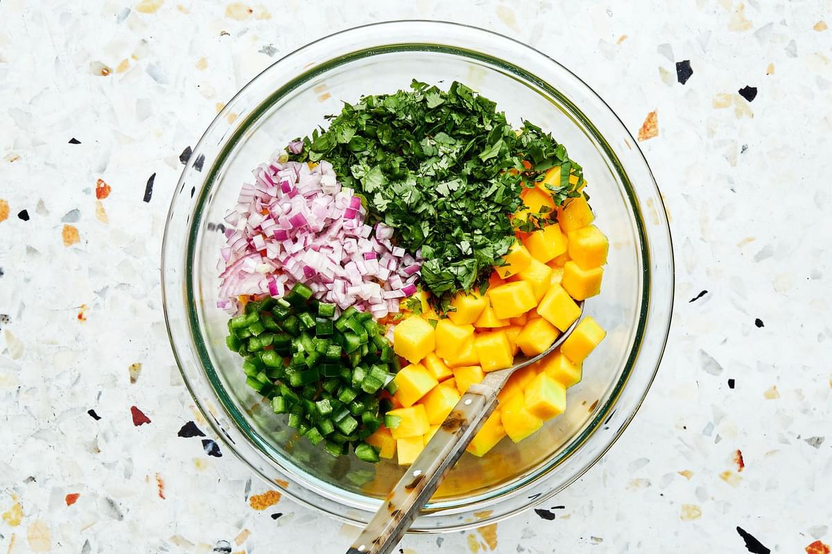 diced mangos, cilantro, red onion and jalapeño in a mixing bowl with a spoon for homemade mango salsa