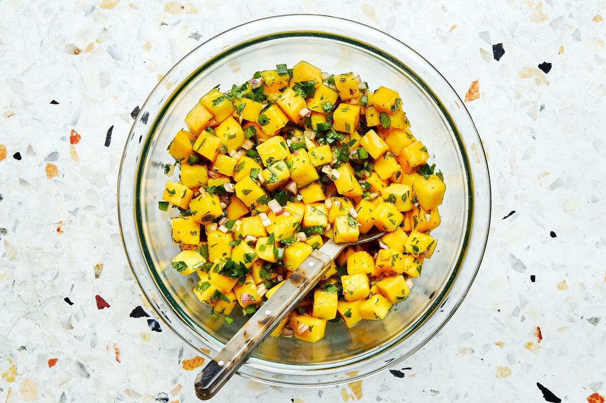 mango salsa in a bowl with a spoon made with mango, red onion, cilantro, jalapeño, lime juice, salt and brown sugar