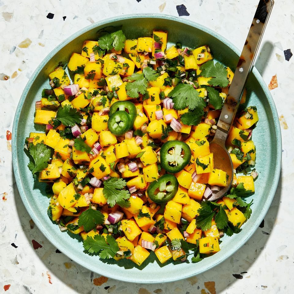 mango salsa in a bowl with a spoon made with mango, red onion, cilantro, jalapeño, lime juice, salt and brown sugar