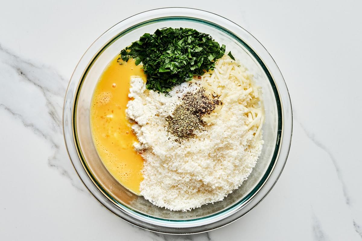ricotta, mozzarella, parmesan, eggs, parsley, garlic clove, Italian seasoning, salt and pepper in a mixing bowl