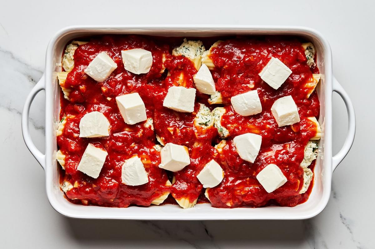 stuffed manicotti noodles in a baking dish covered with marinara sauce and topped with dollops of fresh mozzarella