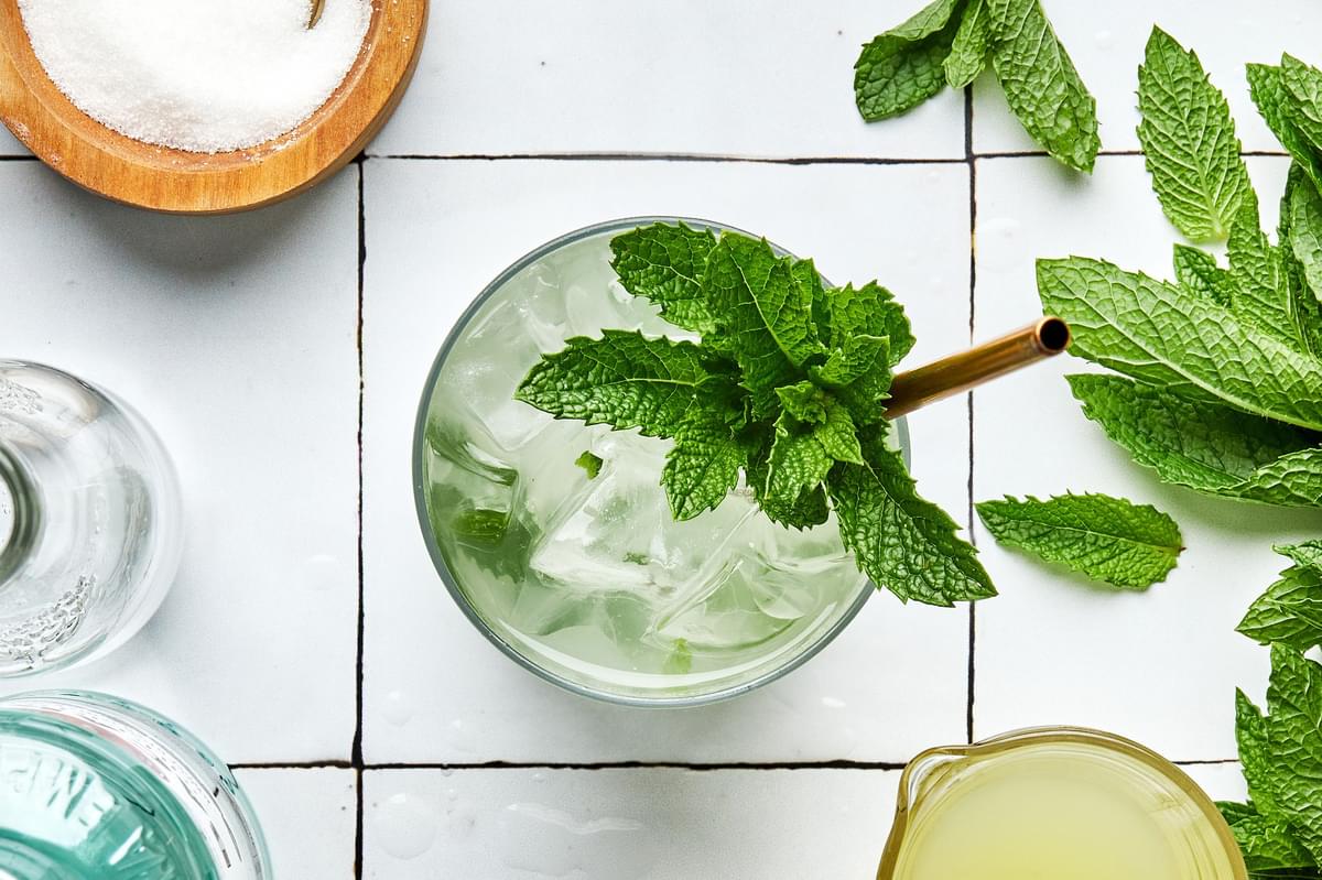 A mojito over ice made with lime juice,  sugar, mint, rum and soda water garnished with fresh mint leaves and lime wedge