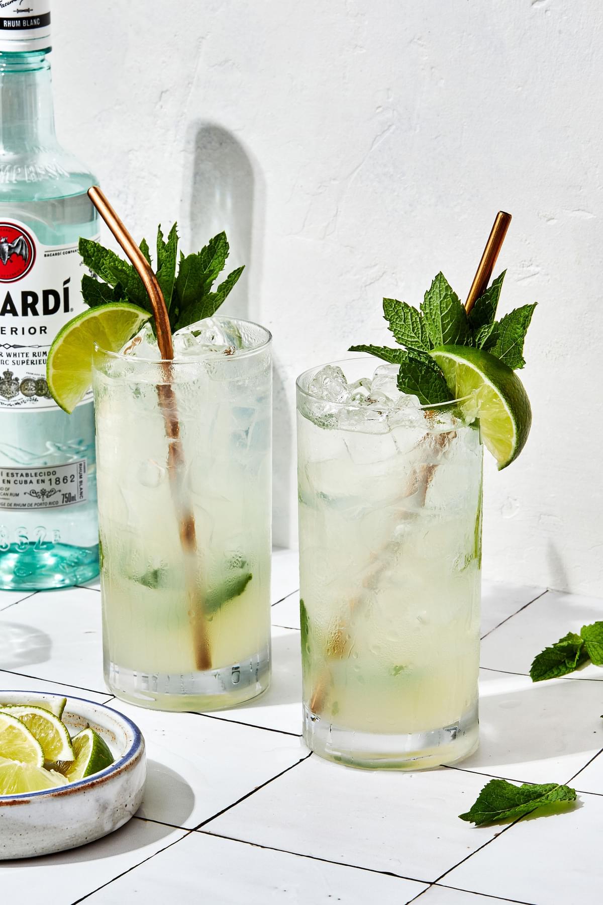 2 Mojitos over ice made with lime juice, sugar, mint, rum and soda water garnished with fresh mint leaves and lime wedge