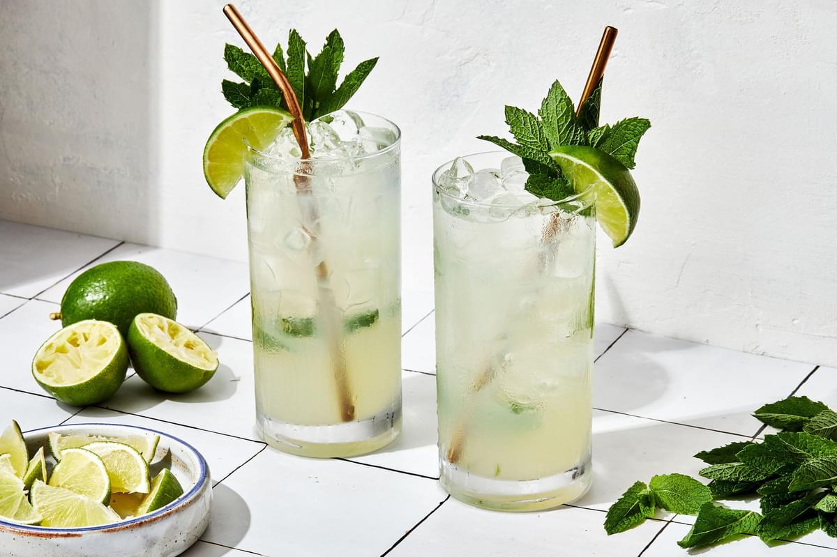 2 Mojitos over ice made with lime juice,  sugar, mint, rum and soda water garnished with fresh mint leaves and lime wedge