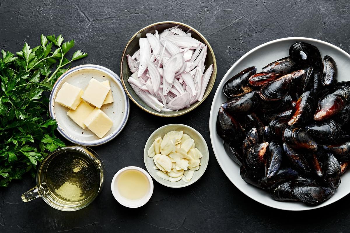 mussels, butter, shallots, garlic, white wine, lemon juice and parsley in bowls to make mussels in wine sauce