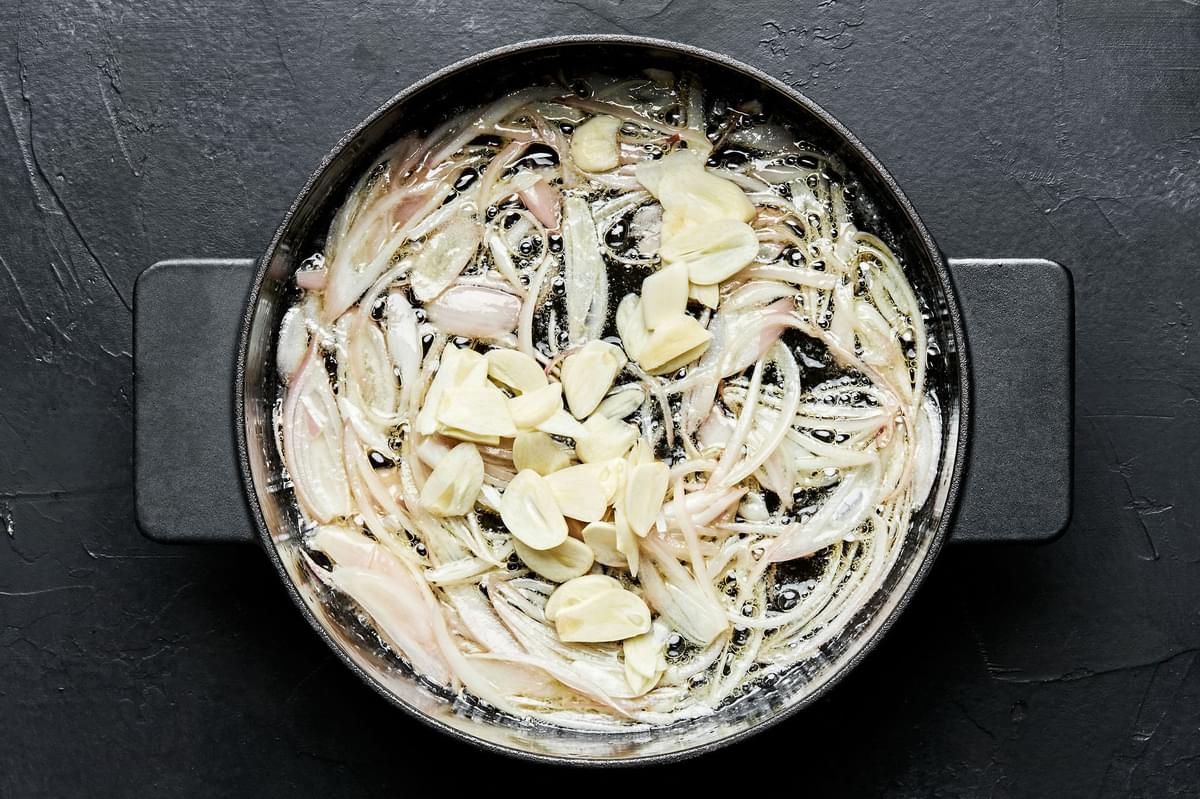 garlic cloves and sliced shallots being cooked in melted butter in a soup pot