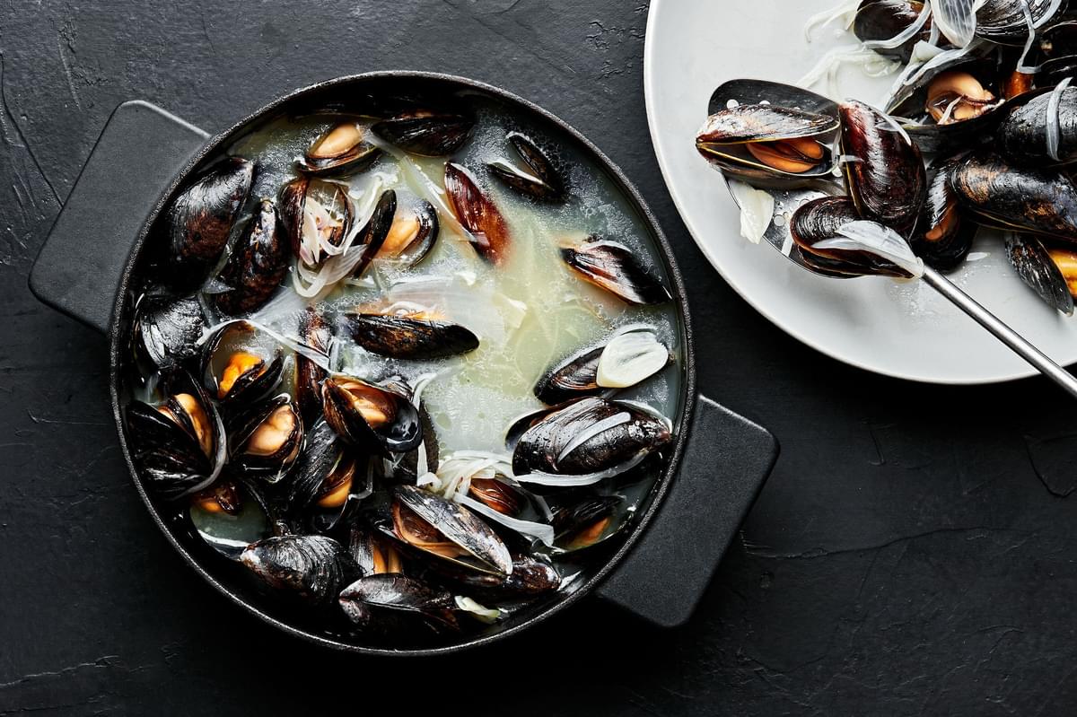 cooked mussels being removed from a soup pot with a slotted spoon