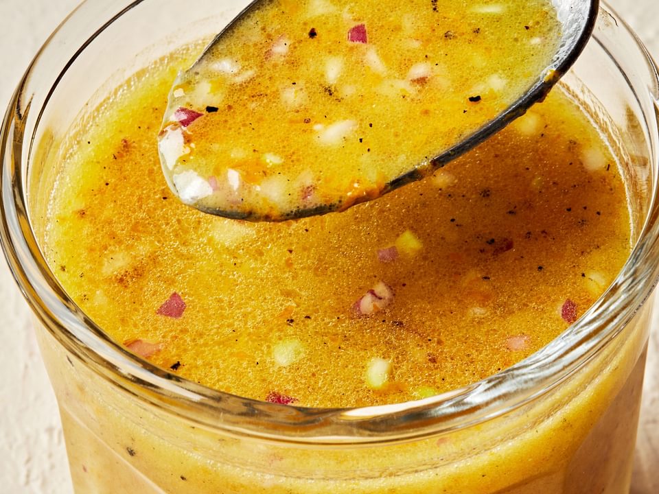 homemade orange vinaigrette in a dish with a spoon made with vinegar, olive oil orange juice, dijon, shallots, salt & pepper