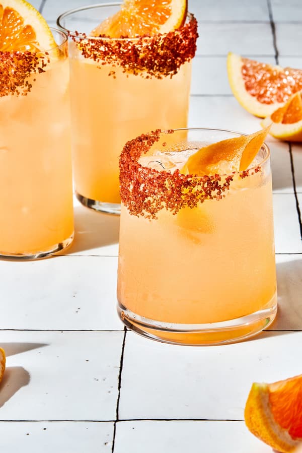 three homemade Palomas in a salt rimmed glasses over ice garnished with grapefruit wedges with extra wedges on the counter