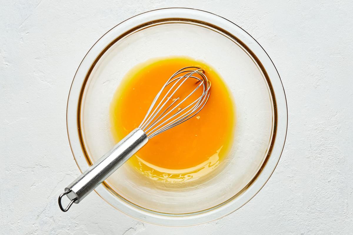 eggs yolks being beat in a glass bowl with a whisk until smooth