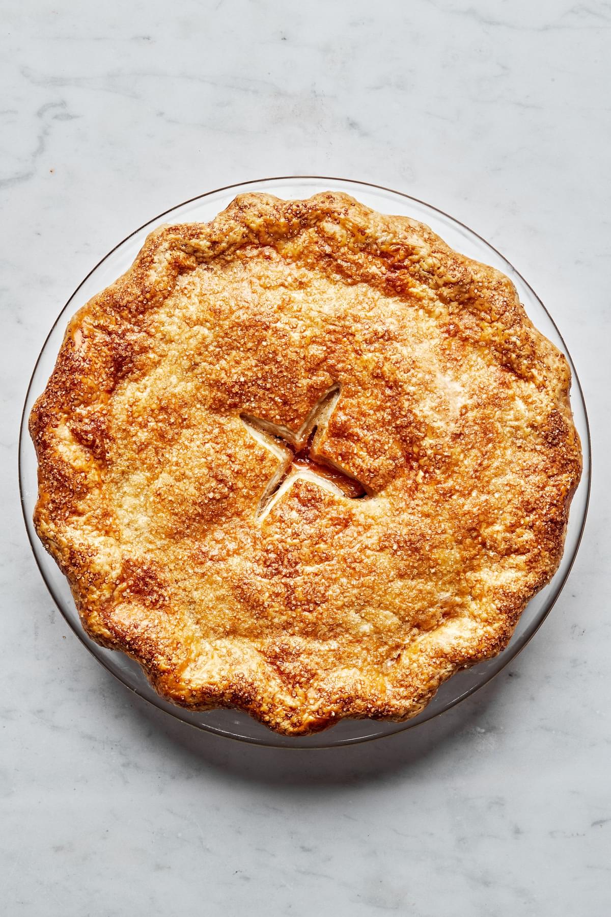 a homemade baked peach pie with brown flaky crust and sprinkled with raw sugar on top