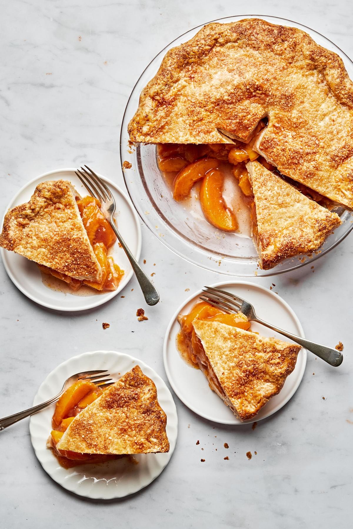 a homemade peach pie with a few slices cut out next to slices of peach pie on plates with forks