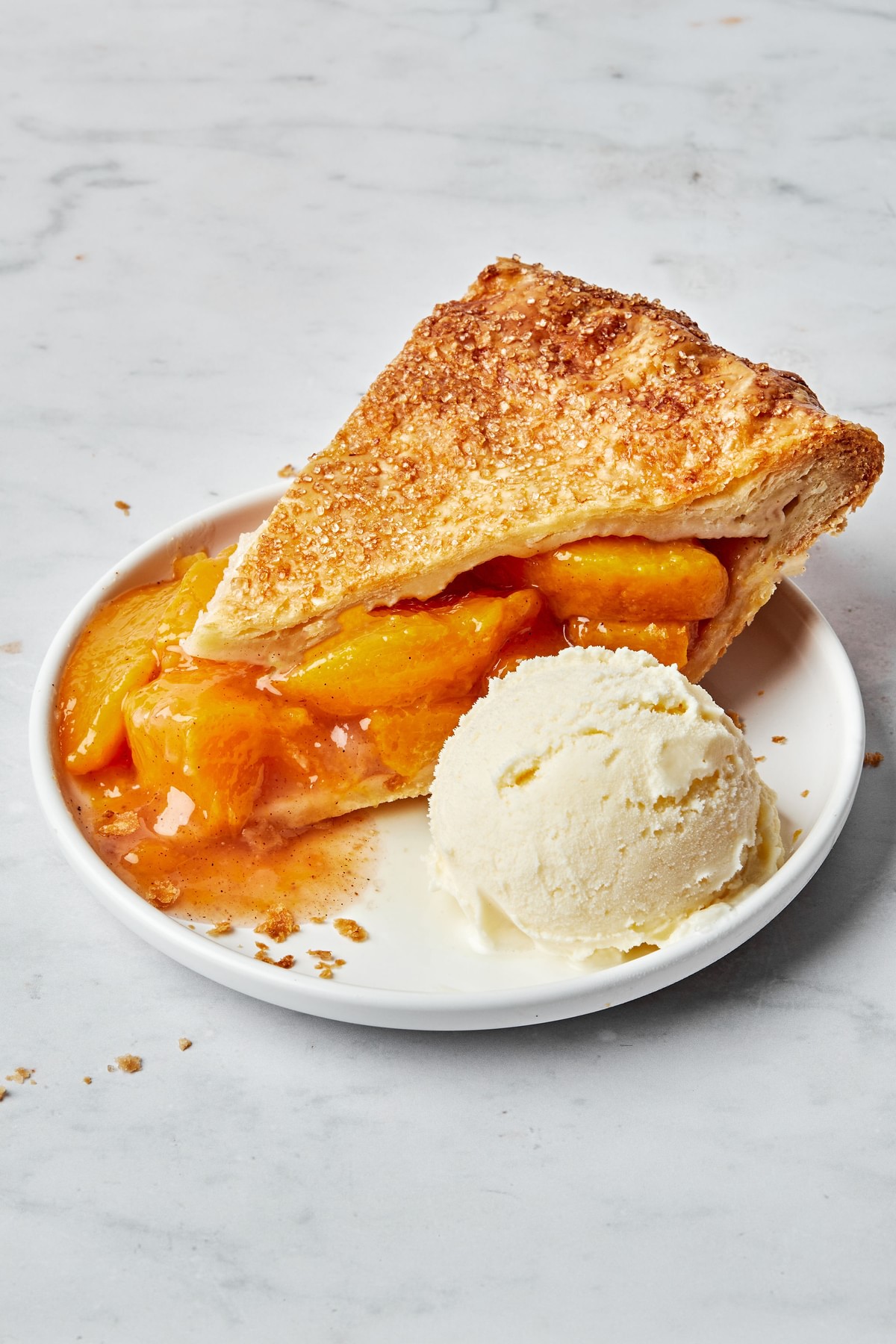 a slice of homemade peach pie with homemade pie crust on a plate with a scoop of vanilla ice cream