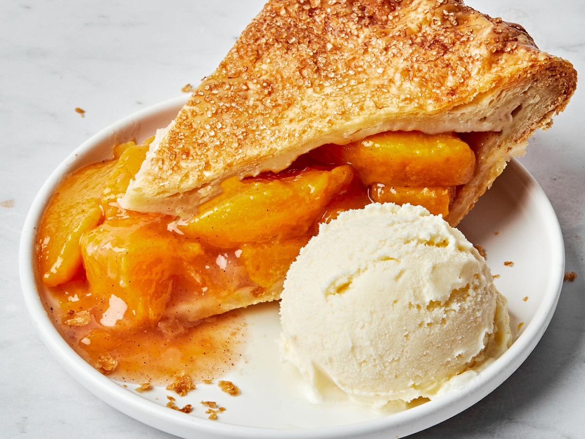 a slice of homemade peach pie with homemade pie crust on a plate with a scoop of vanilla ice cream