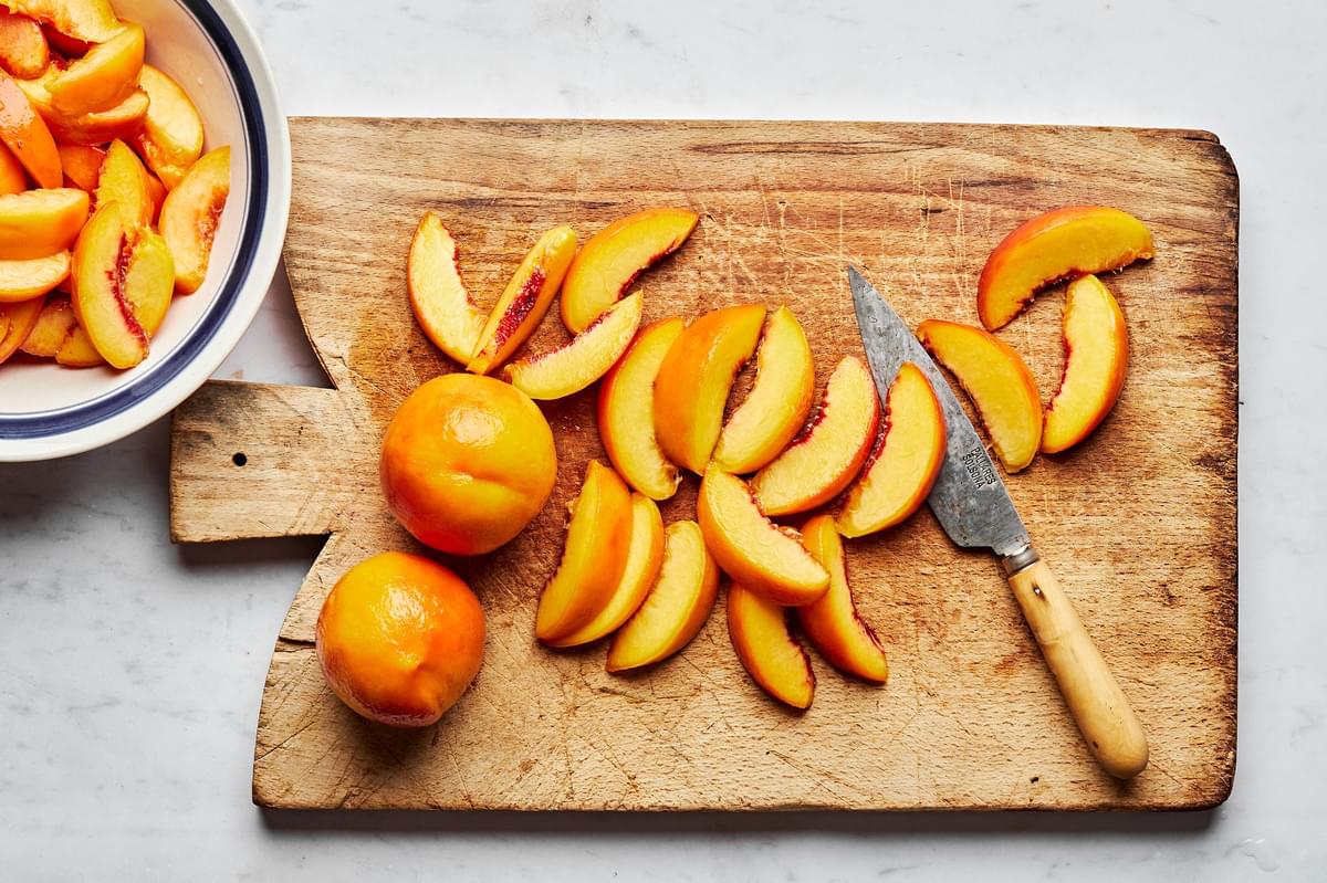 blanched, peeled peaches sliced into wedges on a cutting board for homemade peach pie