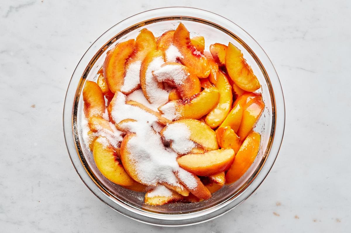 blanched, peeled, sliced peaches being tossed in a bowl with sugar for peach pie