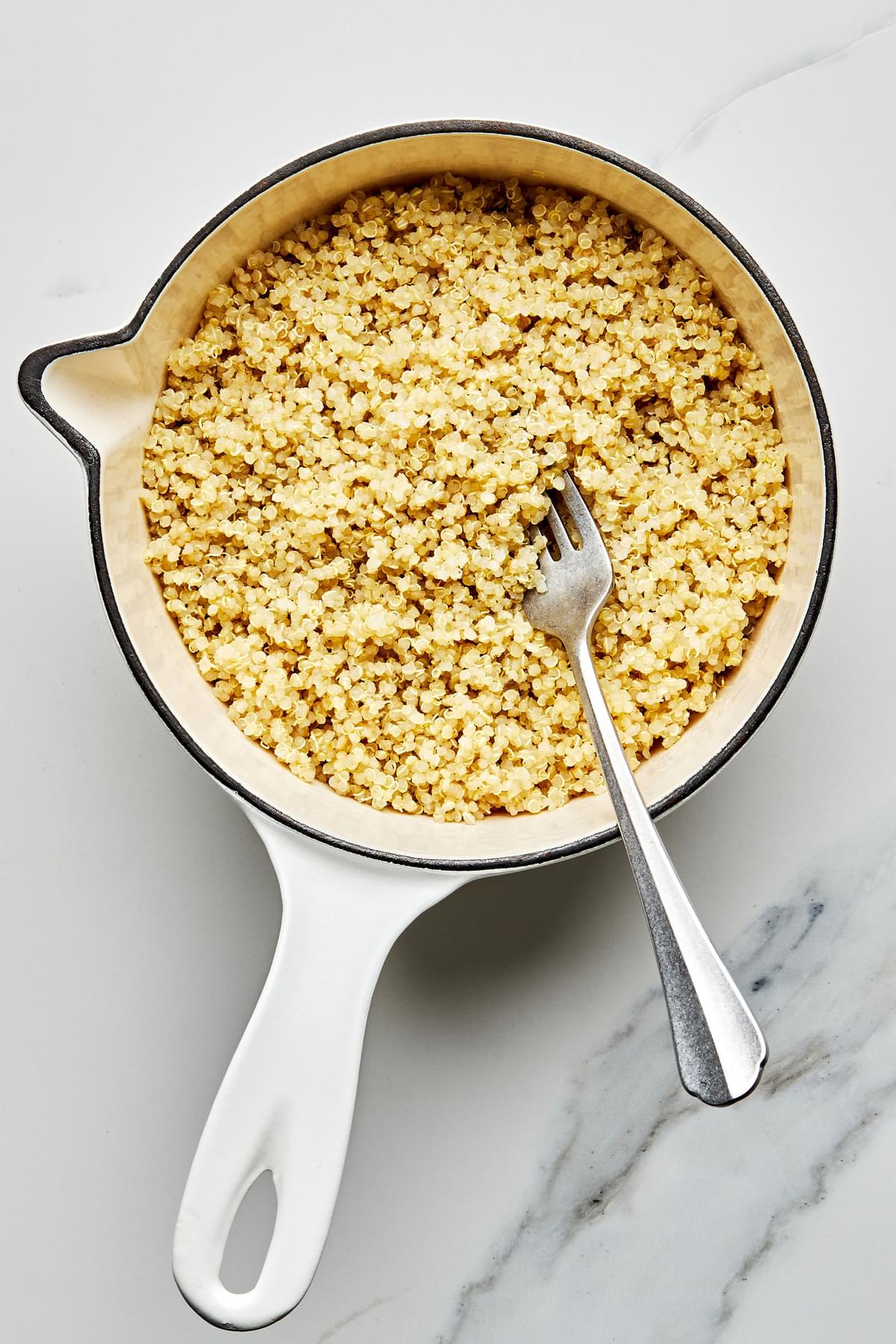 perfectly cooked, fluffy, white quinoa in a small sauce pan being fluffed with a fork