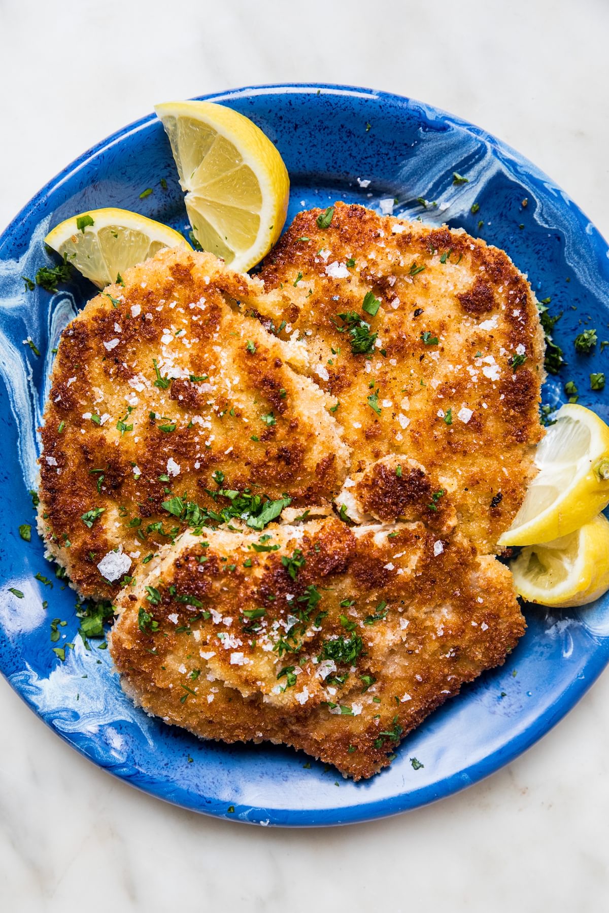 homemade pork schnitzel made with salt, pepper, flour, egg and plain breadcrumbs on a plate with lemon wedges for serving
