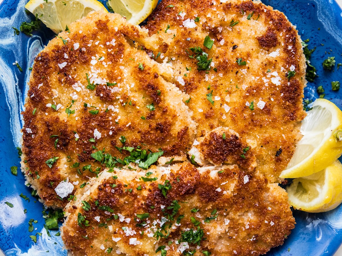homemade pork schnitzel made with salt, pepper, flour, egg and plain breadcrumbs on a plate with lemon wedges for serving