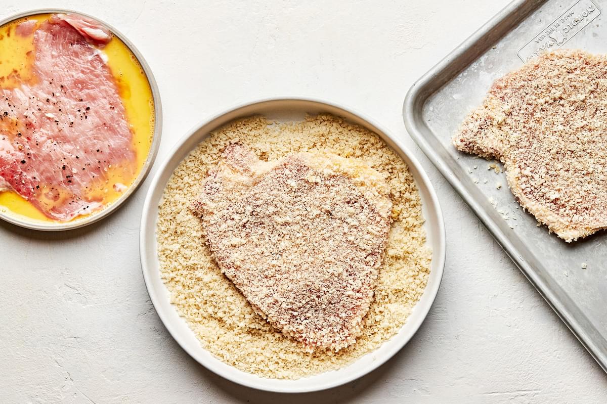 raw pounded pork chops being breaded in egg wash then panko