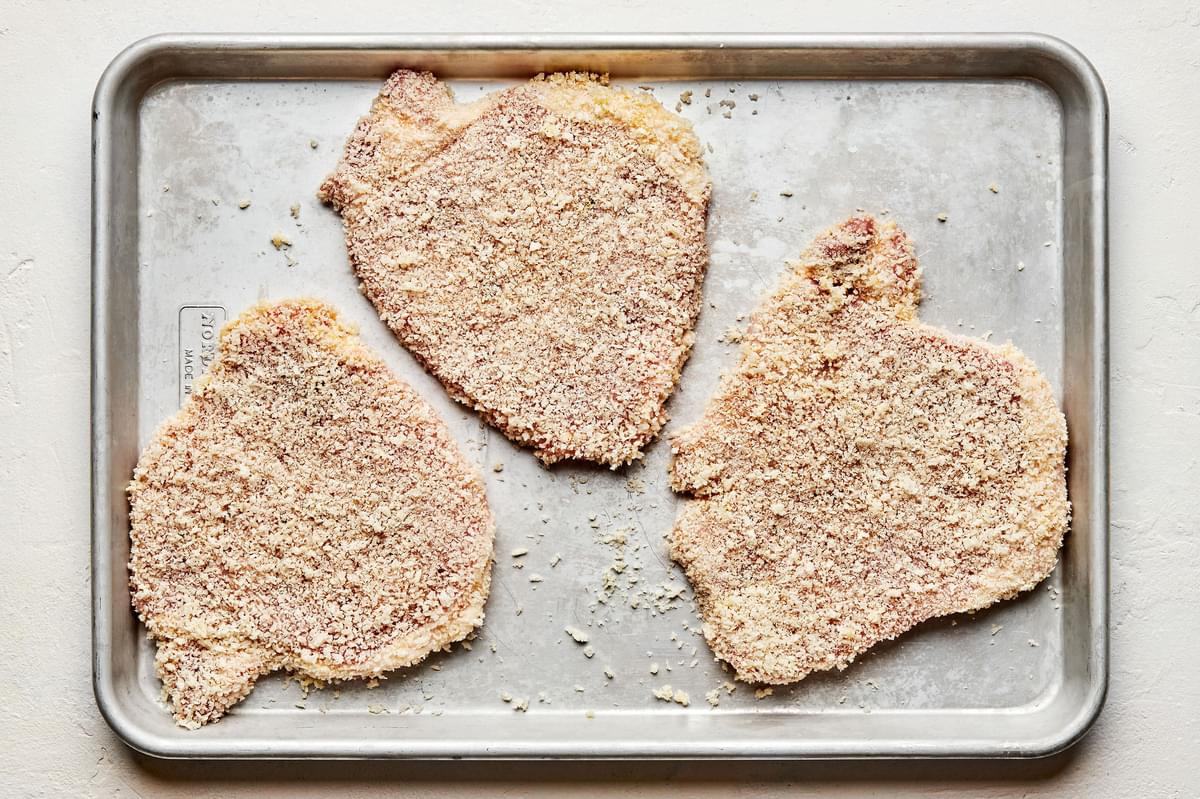 raw pork chops breaded with egg wash and panko on a baking sheet ready to be pan-fried