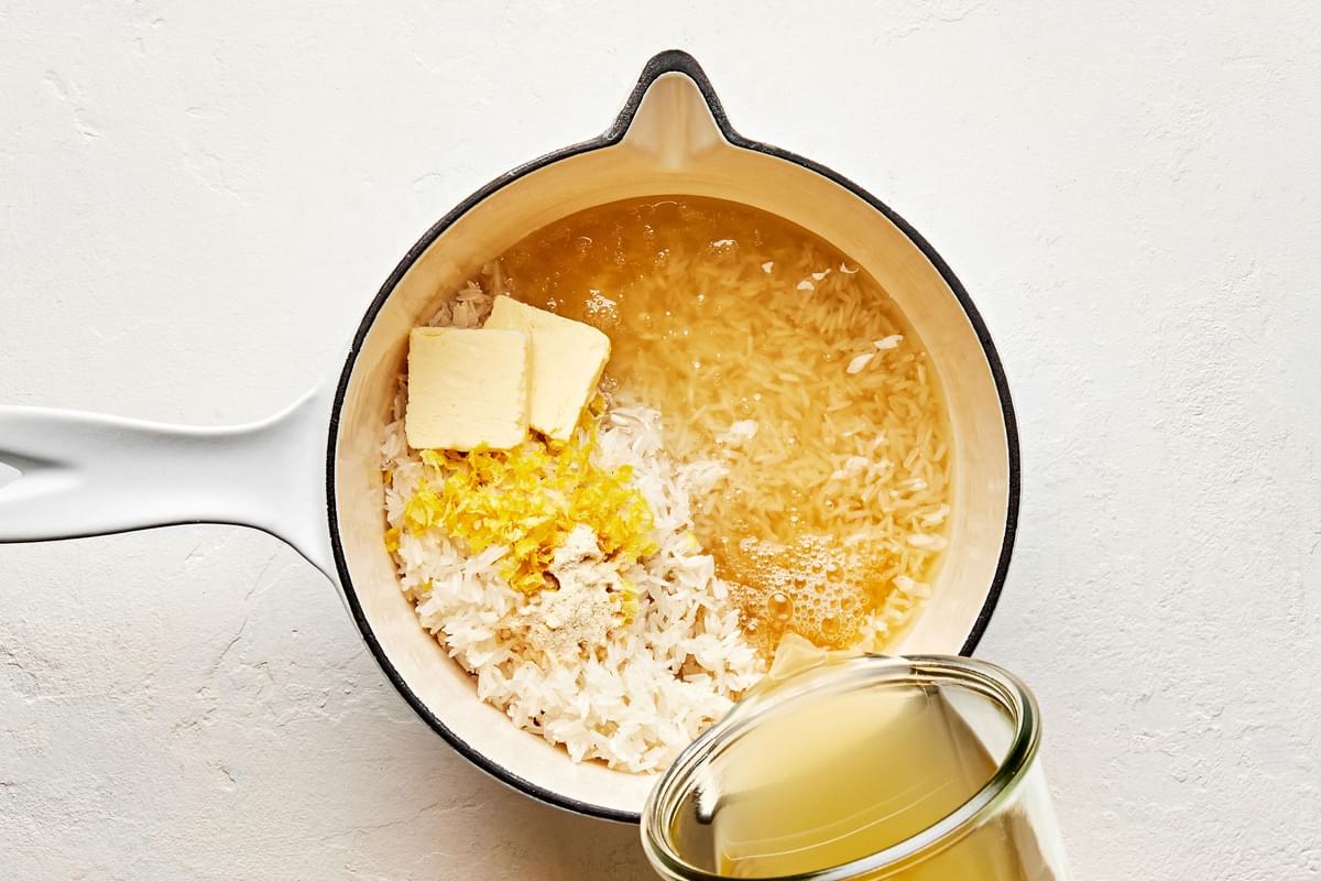 rice, chicken broth, garlic powder, lemon zest & juice & butter being added to a pot to make lemon parmesan rice