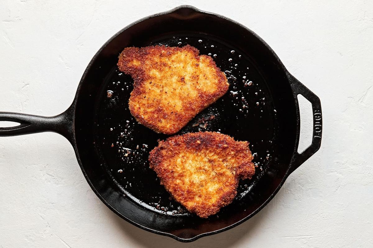 panko coated boneless pork chops being pan-fried in a skillet to use for pork milanese bowls