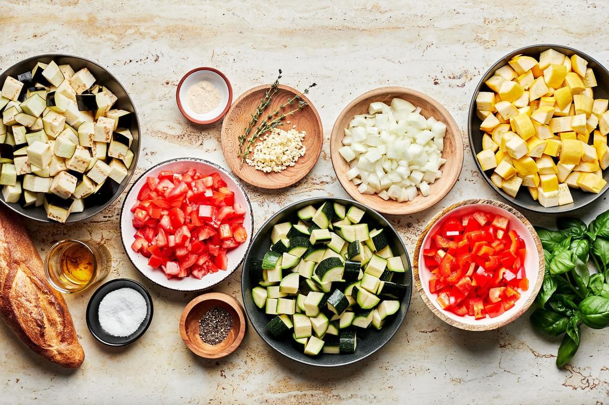 diced eggplant, zucchini, squash, onion, garlic, thyme, tomatoes, peppers, basil, salt and pepper in bowls for ratatouille