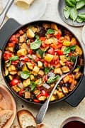 homemade ratatouille in a skillet with a spoon made with diced vegetables, spices, olive oil and fresh basil