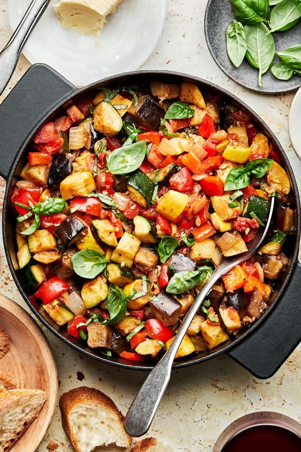 homemade ratatouille in a skillet with a spoon made with diced vegetables, spices, olive oil and fresh basil