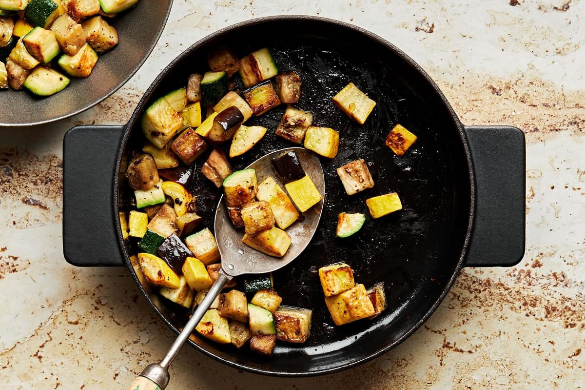 eggplant, zucchini and squash seasoned with salt and pepper being cooked in a skillet with olive oil